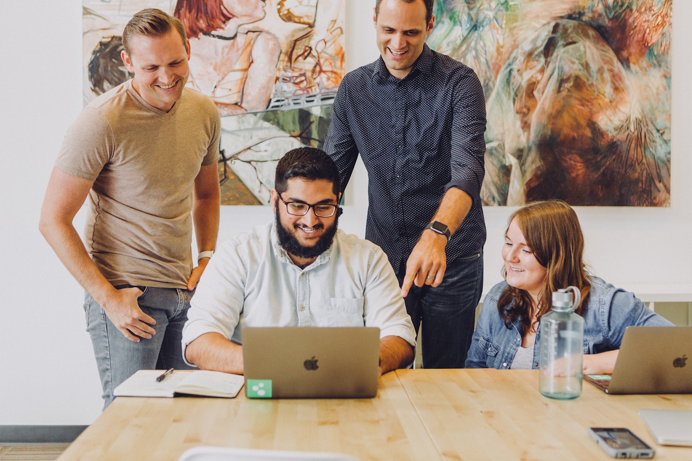 A team of colleagues smiling and collaborating around a laptop